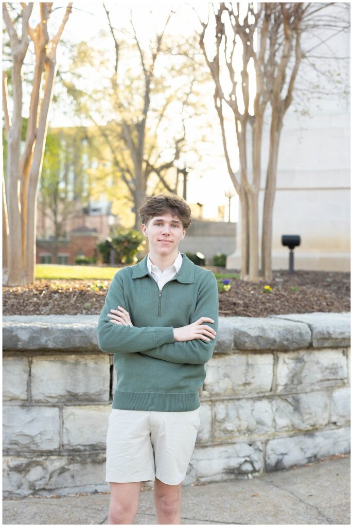 senior guy crossing his arms and posing in front of a stone wall and trees in Chattanooga