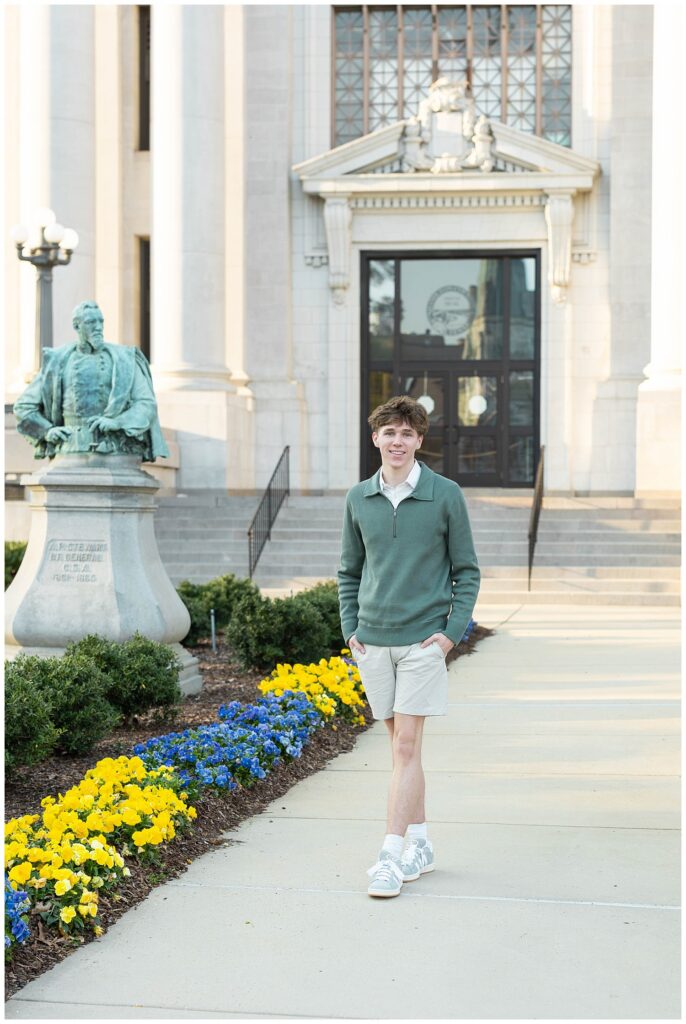 senior guy wearing a green sweater and shorts walking on the sidewalk next to flowers in Chattanooga