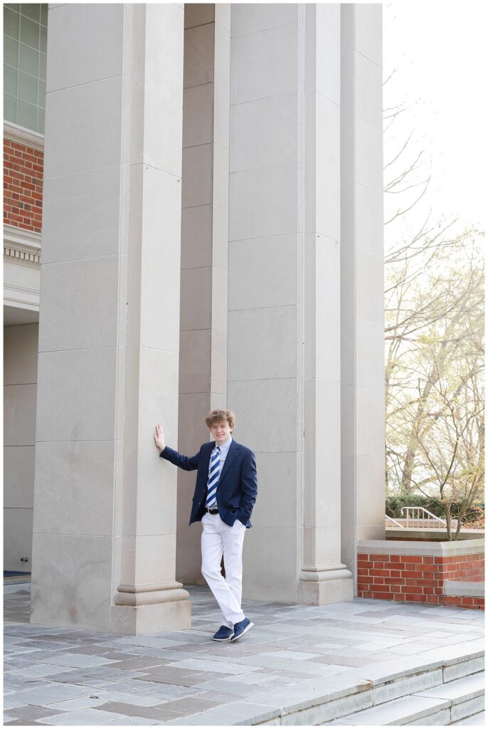 high school senior wearing a blue blazer leaning against a tall column at McCallie School